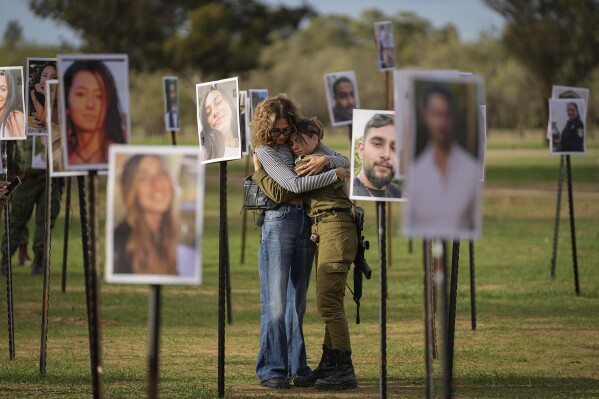 Israelis embrace next to photos of people killed and taken captive by Hamas militants during their violent rampage through the Nova music festival in southern Israel, which are displayed at the site of the event near kibbutz Re'im, Tuesday, Nov. 28, 2023. (AP Photo/Ohad Zwigenberg)