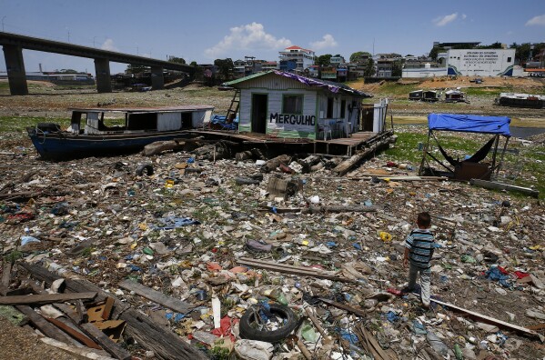 Boys walk next to a floating home stranded on what used to be the water's edge of the Negro river, amidst a drought in Manaus, Brazil, Tuesday, Sept. 26, 2023. The Brazilian Amazon rainforest is facing a severe drought that may affect around half a million people by the end of the year, authorities said Tuesday. (AP Photo/Edmar Barros)