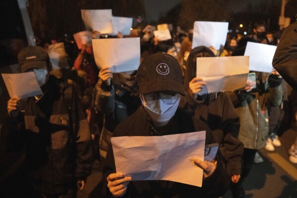 FILE - Protesters hold up blank pieces of paper and chant slogans as they march to protest strict anti-virus measures in Beijing, Nov. 27, 2022. Thousands of people demonstrated across China in what came to be called the White Paper movement, after the blank sheets of paper protesters used to represent the country's strict censorship controls. One year later, China has all but forgotten the protests. The state reacted quickly, breaking up the marches with arrests and threats and ending COVID-19 controls. (AP Photo/Ng Han Guan, File)