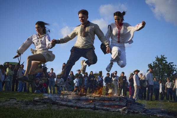 People jump over bonfire during a traditional midsummer celebration in Pyrohiv, Ukraine, outside of Kyiv, Saturday, June 21, 2025. (AP Photo/Efrem Lukatsky)