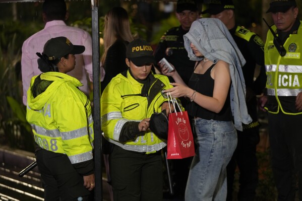 Police ask a woman for proof of age at a checkpoint at an entrance to Lleras Park during an operation to enforce a curfew for minors in Medellin, Colombia, Friday, Feb. 2, 2024. The city has imposed an evening curfew on minors, as part of its efforts to reduce sex trafficking. (AP Photo/Fernando Vergara)