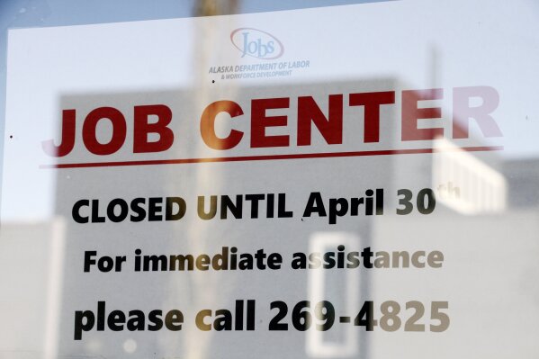 In this March 30, 2020 photo, a sign saying that the Jobs Center at the Alaska Department of Labor and Workforce Development office in midtown Anchorage, Alaska, is closed through the end of April is shown. About half of all working Americans say they or a member of their household have lost some kind of income due to the coronavirus pandemic, with low-income Americans and those without college degrees especially likely to have lost a job. That's according to a new poll from The Associated Press-NORC Center for Public Affairs Research.  (AP Photo/Mark Thiessen)