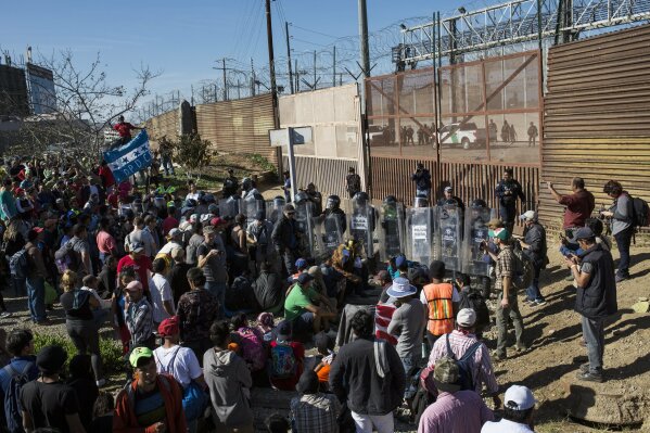 
              Migrants stand at the Mexico-U.S. border wall where Mexican federal police stand guard at the Chaparral crossing in Tijuana, Mexico, Sunday, Nov. 25, 2018, as they try to reach the U.S. The mayor of Tijuana has declared a humanitarian crisis in his border city and says that he has asked the United Nations for aid to deal with the approximately 5,000 Central American migrants who have arrived in the city. (AP Photo/Rodrigo Abd)
            