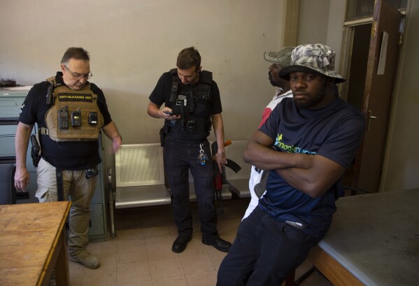Two men, on right, suspected of driving a stolen vehicle, are handed over to police by private security personal, Anton Koen, left, in a suburb east of Johannesburg, South Africa, Friday, Dec. 1, 2023. (AP Photo/Denis Farrell)
