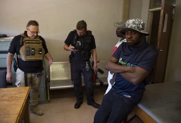 Two men, on the right, are handed over to police by private security guard Anton Koen, on the left, on suspicion of driving a stolen vehicle, in a suburb east of Johannesburg, South Africa, Friday, Dec. 1, 2023.  (AP Photo/Dennis Farrell)