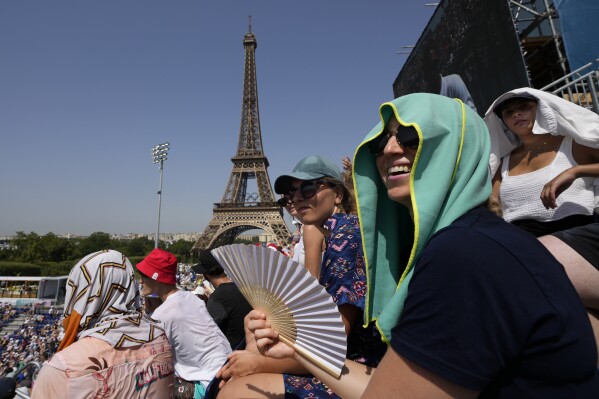 Stephanie Touissaint, foreground, uses a fan to keep cool in the sweltering heat at Eiffel Tower Stadium during a beach volleyball match between Cuba and Brazil at the 2024 Summer Olympics, July 30, 2024, in Paris, France. (AP Photo/Robert F. Bukaty, File)