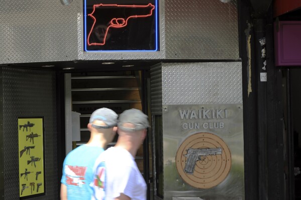 FILE - People walk past a gun club on June, 23, 2022, in Honolulu. A ruling by Hawaii's high court saying that a man can be prosecuted for carrying a gun in public without a permit uses pop culture references in an apparent rebuke of a U.S. Supreme Court decision that expanded gun rights nationwide. (AP Photo/Marco Garcia, File)