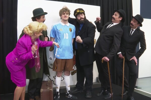 In this grab made from video, a model wearing Belgium's jersey poses with actors impersonating characters from Tintin during the unveiling of the new Belgium soccer national team jersey, in Brussels, Belgium, Thursday, March 14, 2024. (SNTV via AP)