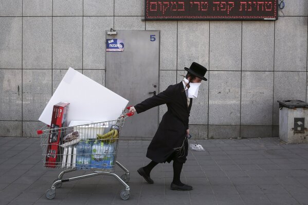 An ultra-Orthodox Jew wears an improvised protective face mask as he pulls a supermarket cart on a mainly deserted street because of the government's measures to help stop the spread of the coronavirus, in Bnei Brak, a suburb of Tel Aviv, Israel, Friday, April 3, 2020.   The military plans to send troops in to assist local authorities with coronavirus control.   (AP Photo/Oded Balilty)