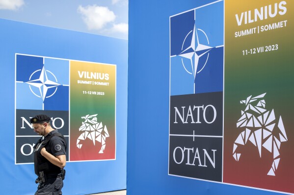 FILE - A security guard walks in front of a banner outside the venue of the NATO summit in Vilnius, Lithuania, July 9, 2023. When Sweden applied for NATO membership together with Finland, both expected a quick accession process, but more than a year later Sweden is still in the alliance's waiting room. New entries must be approved by all existing members and as NATO leaders meet for a summit in Vilnius, Sweden is missing the green light from two: Turkey and Hungary. (AP Photo/Mindaugas Kulbis, File)