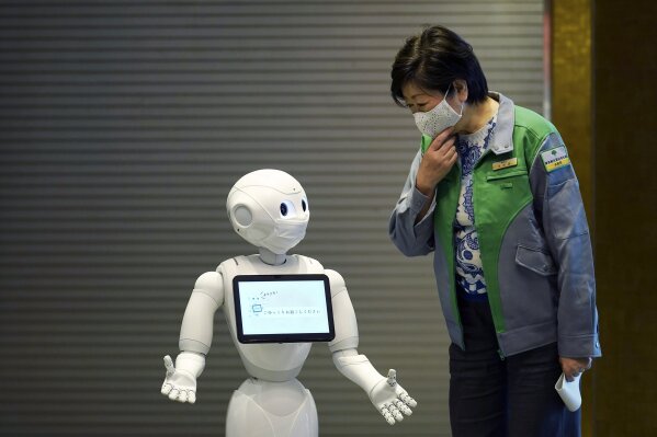 A humanoid robot Pepper wearing a face mask greets Tokyo Gov. Yuriko Koike at the lobby of a hotel for the new coronavirus COVID-19 patients with mild symptoms during a media preview in Tokyo Friday, May 1, 2020. Prime Minister Shinzo Abe said Thursday he planned to extend a state of emergency beyond the scheduled end of May 6 because infections are spreading and hospitals are overburdened. (AP Photo/Eugene Hoshiko)