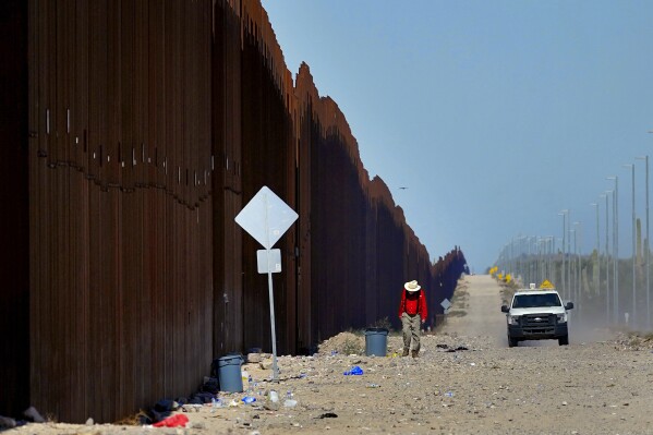 FILE - Retired schoolteacher Tom Wingo, of Samaritans Without Borders, walks on the Roosevelt Easement picking up trash along the border fence as a U.S. Customs and Border Patrol agent patrols the area, Aug. 29, 2023, in Organ Pipe Cactus National Monument near Lukeville, Ariz. On Monday, Nov. 27, Customs and Border Protection said it was closing one of two bridges to vehicles in Eagle Pass, Texas, a town of about 30,000 people that, for a while last year, was the busiest corridor for illegal crossings. It is also reducing vehicle entries in Lukeville, a remote desert crossing that has become a major migration route in recent months. (AP Photo/Matt York, File)