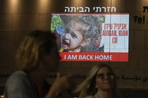 FILE - People walk past an image of 4-year-old Abigail Edan, a hostage held by Hamas, projected onto a building in Tel Aviv, Nov 26, 2023. Edan's parents were both killed by Hamas militants in the same attack in which she was kidnapped, a cross-border assault Oct. 7 that prompted Israel to declare war on Hamas. President Joe Biden has met at the White House with Abigail Edan. (AP Photo/Ariel Schalit, File)