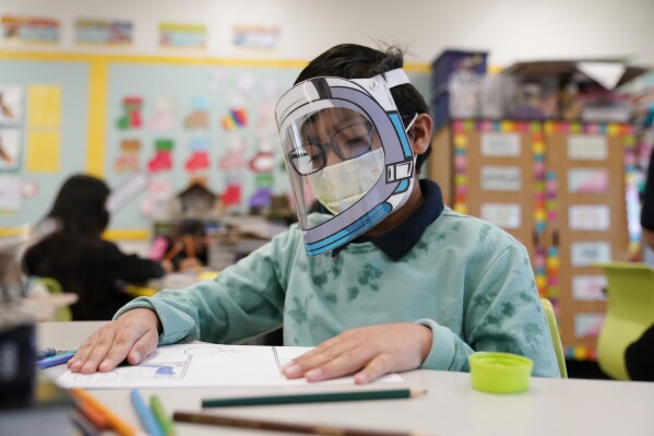 FILE - A student wears a mask and face shield in a 4th grade class amid the COVID-19 pandemic at Washington Elementary School on Jan. 12, 2022, in Lynwood, Calif. Four years after the COVID-19 pandemic closed schools and upended child care, the CDC says parents can start treating the virus like other respiratory illnesses. (APPhoto/Marcio Jose Sanchez, File)