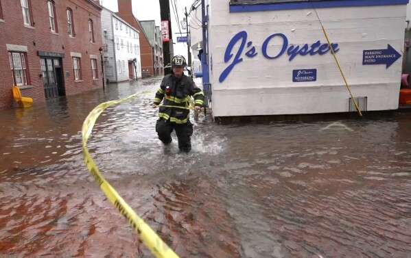 FILE - Wind whips caution tape as a firefighter closes off a flooded waterfront street during a severe storm in this Jan. 10, 2024, in Portland, Maine. (AP Photo/Robert F. Bukaty)