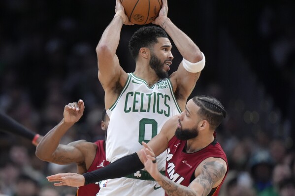 Boston Celtics forward Jayson Tatum, center, passes the ball over Miami Heat forward Caleb Martin, right, in the second half of Game 1 of an NBA basketball first-round playoff series, Sunday, April 21, 2024, in Boston. (AP Photo/Steven Senne)