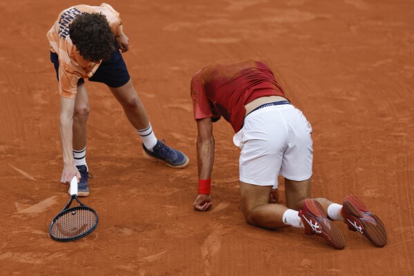 A ball kid came to the aid of Serbia's Novak Djokovic after he slipped and fell during his fourth round match of the French Open tennis tournament against Argentina's Francisco Cerundolo at the Roland Garros stadium in Paris, Monday, June 3, 2024. (AP Photo/Jean-Francois Badias)