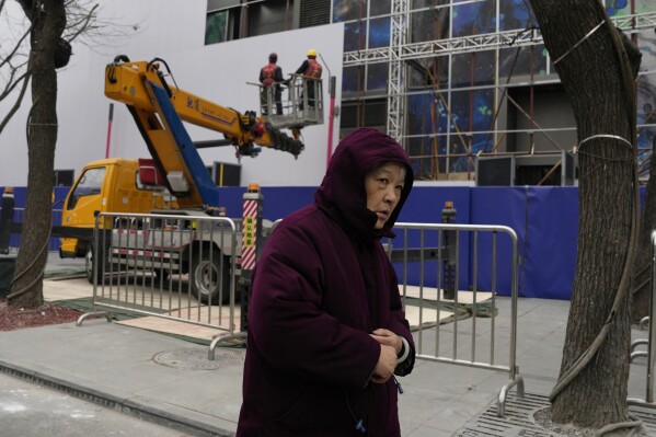 An elderly woman passes by workers dismantling scaffolding at a shopping mall in Beijing, Wednesday, Jan. 17, 2024. China's economy for the October-December quarter grew at a quicker rate, allowing the Chinese government to hit its target of about 5% annual growth for 2023 even though trade data and the economic recovery remain uneven. (AP Photo/Ng Han Guan)