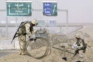 FILE - U.S. Army troops clear rolls of razor wire from the main entrance to Fallujah, Iraq, April 30, 2004. The Navy's next amphibious assault ship will be named after the city of Fallujah, which saw some of the bloodiest battles in the Iraq war when U.S. Marines fought al-Qaida extremist in deadly house-to-house combat. (AP Photo/Anja Niedringhaus, File)