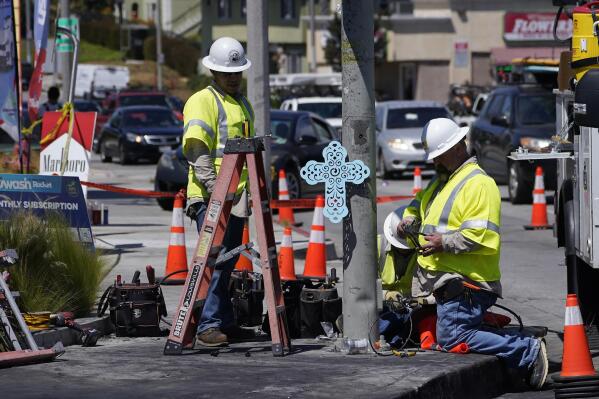 A memorial cross is posted on a traffic pole as Los Angeles City Public Works technicians replace burned traffic lights and signs after crash involving multiple cars near a gas station in the unincorporated Windsor Hills in Los Angeles on Friday, Aug. 5, 2022. A speeding car ran a red light and plowed into cars in a crowded intersection Thursday in a fiery crash that killed several people, including a baby, just outside of Los Angeles, authorities said. (AP Photo/Damian Dovarganes)