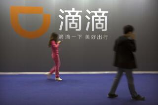 FILE - In this April 27, 2017 file photo, visitors walk past a sign for Chinese ride-hailing service Didi Chuxing at the Global Mobile Internet Conference (GMIC) in Beijing.   Chinese regulators have clamped down on the country’s largest ride-hailing app, Didi Global Inc., days after its shares began trading in New York. Authorities told Didi to stop new registrations and ordered its app removed from China’s app stores pending a cybersecurity review.  (AP Photo/Mark Schiefelbein, File)