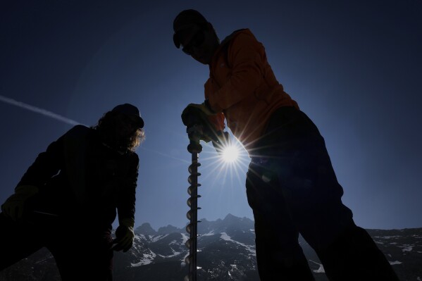 Matthias Huss, of the Federal Institute of Technology in Zurich and glacier monitoring group GLAMOS, right, drills holes into the Rhone Glacier near Goms, Switzerland, June 10, 2025. (AP Photo/Matthias Schrader)
