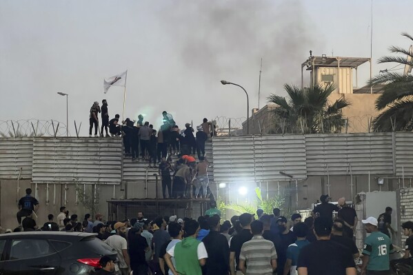 CORRECTS SECOND SENTENCE - Protesters scale a wall at the Swedish Embassy in Baghdad Thursday, July 20, 2023. Protesters angered by the planned burning of a copy of the Quran stormed the embassy early Thursday, breaking into the compound and lighting a small fire. (AP Photo/Ali Jabar)