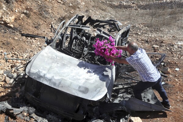 Samir Ayoub, uncle of three children who were killed by an Israeli airstrike, puts flowers on their car in the town of Ainata, a Lebanese border village with Israel in south Lebanon, Monday, Nov. 6, 2023. An Israeli airstrike in south Lebanon on Sunday, Nov. 5, 2023 evening killed four civilians, including a woman and three children, raising the likelihood of a dangerous new escalation in the conflict on the Lebanon-Israel border. (AP Photo/Mohammed Zaatari)