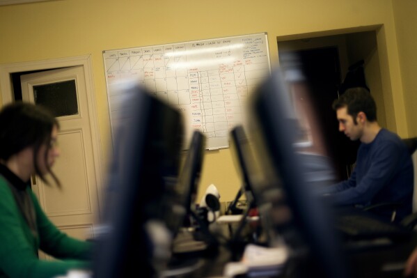 FILE - A billboard with working schedules hangs from the wall as Mar Parreno, left, and Mario Perez, two of the founders of the Factoria 5 digital design company, work in their office in Madrid, Monday, Feb. 25, 2013. The parties forming Spain’s acting government said Tuesday, Oct. 24, 2023, they will push for a 37½-hour workweek as part of an agreement the coalition partners struck as they try to remain in power following an inconclusive election in July. Spain has had a 40-work week for the past two decades. (AP Photo/Daniel Ochoa de Olza, File)