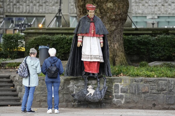 People stand at the monument of German cardinal Franz Hengsbach beside the cathedral in the city center of Essen, western Germany, Friday, Sept. 22, 2023. The Catholic Church is investigating allegations of sexual abuse by the late cardinal over 30 years after his death. (AP Photo/Martin Meissner)