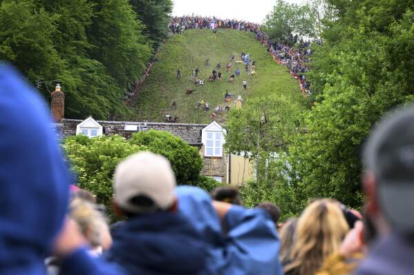 Spectators watch participants competing in the men's downhill race category of the traditional annual Cheese Rolling contest at Cooper's Hill in Brockworth, Gloucestershire, England, Monday, May 26, 2025.(AP Photo/Anthony Upton)