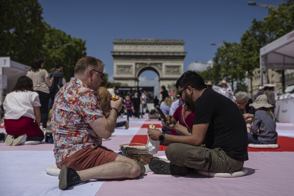 People eat their lunches as part of a giant picnic on the Champs-Elysées, in front of the Arc de Triomphe, organized by the Comité Champs-Élysées, Sunday, May 26, 2024 in Paris. (AP Photo/Aurelien Morissard)