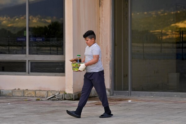 A boy displaced from his home in southern Lebanon by clashes on the border with Israel carries food distributed to displaced families at a hotel being used as a shelter in the southern town of Marwanieh, Lebanon, Friday, March 15, 2024. (AP Photo/Bilal Hussein)