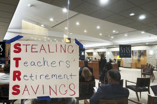 A poster using the initials of the State Teachers Retirement System of Ohio to spell out "Stealing Teachers' Retirement Savings" hangs on the wall during a board meeting at the pension fund's headquarters in Columbus, Ohio, on Wednesday, May 15, 2024. (AP Photo/Julie Carr Smyth)