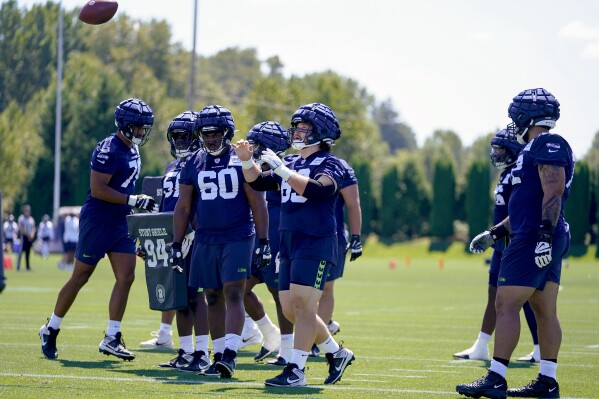 CORRESCTS THE NAME OF THE PLAYER TOSSING THE BALL TO EVAN BROWN (63) NOT JACOB SYKES (69) AS ORIGNALLY SENT - Seattle Seahawks center Evan Brown tosses a ball as guard Phil Haynes (60) and other defensive players watch during the NFL football team's training camp Wednesday, July 26, 2023, in Renton, Wash. (AP Photo/Lindsey Wasson)