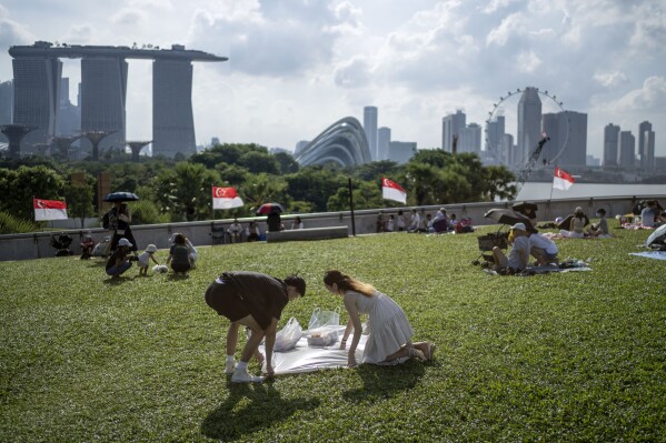 A couple spreads a blanket for a picnic on the grassy roof of the Marina Barrage pumping station, against the backdrop of the Singapore skyline, Saturday, July 22, 2023. The barrage and the adjacent dam separates seawater to create a freshwater reservoir downtown, the city-state's largest and most urbanized catchment area. (AP Photo/David Goldman)