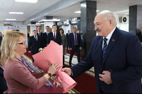 In this photo provided by the Belarusian Presidential Press Service, Belarus President Alexander Lukashenko, right, presents flowers to an election commission official ahead of voting at a polling station, in Minsk, Belarus, Sunday, Feb. 25, 2024. Lukashenko was believed a few years ago to be considering whether to lead the new body after stepping down, but his calculus has apparently changed, and he announced on Sunday that he will run in next year's presidential election. (Belarusian Presidential Press Service via AP)