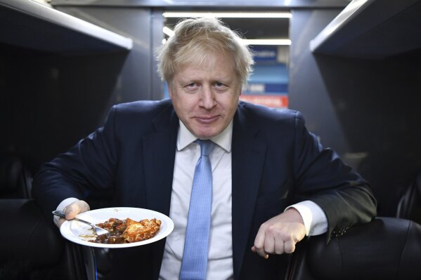 Britain's Prime Minister Boris Johnson eats a portion of pie aboard the Conservative Party campaign bus after a visit to the Red Olive catering company in Derby, central England Wednesday Dec. 11, 2019.  Britain will go to the polls tomorrow Dec. 12, to vote in a pre-Christmas general election. (Ben Stansall/Pool via AP)
