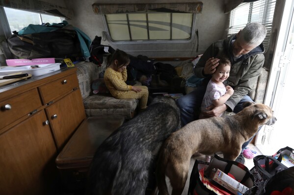 Hazel York, left, looks on as her father Stuart York holds her sister Hannah inside their travel trailer at the evacuation centre in Peace River, Alberta, Aug. 18, 2023. (Jason Franson /The Canadian Press via AP)