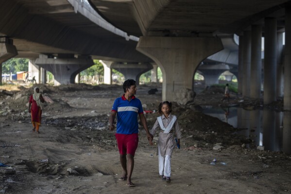 Shiv Kumar, left, accompanies his daughter Garima, 10, to her school as they walk on the flood plain of Yamuna River, in New Delhi, India, Friday, Sept. 29, 2023. (AP Photo/Altaf Qadri)