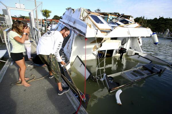 A couple look at a damaged boat in a marina at Tutukaka, New Zealand, Sunday, Jan. 16, 2022, after waves from a volcano eruption swept into the marina. An undersea volcano erupted in spectacular fashion Saturday near the Pacific nation of Tonga, sending tsunami waves crashing across the shore and people rushing to higher ground. (Tanya White/Northern Advcate/NZME via AP)