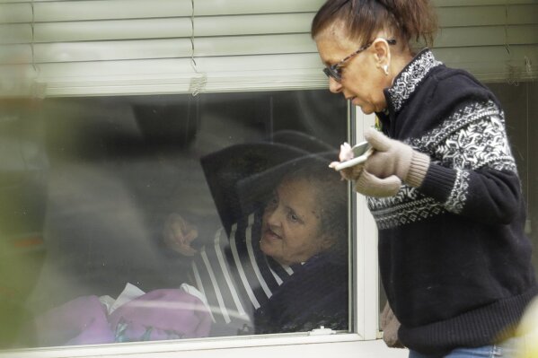 Carmen Gray, right, talks with her mother, Susan Hailey, left, who has tested positive for the new coronavirus, through the window of Hailey's room at the Life Care Center in Kirkland, Wash., Tuesday, March 17, 2020, near Seattle. In-person visits are not allowed at the nursing home, at the center of the outbreak of new coronavirus. (AP Photo/Ted S. Warren)