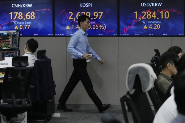 A currency trader passes by screens showing the Korea Composite Stock Price Index (KOSPI), top center, and the foreign exchange rate between U.S. dollar and South Korean won, top right, at the foreign exchange dealing room of the KEB Hana Bank headquarters in Seoul, South Korea, Tuesday, July 25, 2023. Asian stock markets followed Wall Street higher on Tuesday after China's ruling Communist Party promised to shore up its sagging economy ahead of a Federal Reserve meeting traders hope will announce this interest rate cycle's final increase. (AP Photo/Ahn Young-joon)