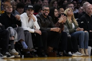 Bad Bunny (centro) observa la segunda mitad del juego de baloncesto de la NBA entre los Warriors de Golden State y los Lakers de Los Ángeles, el sábado 16 de marzo de 2024. (AP Foto/Ashley Landis)