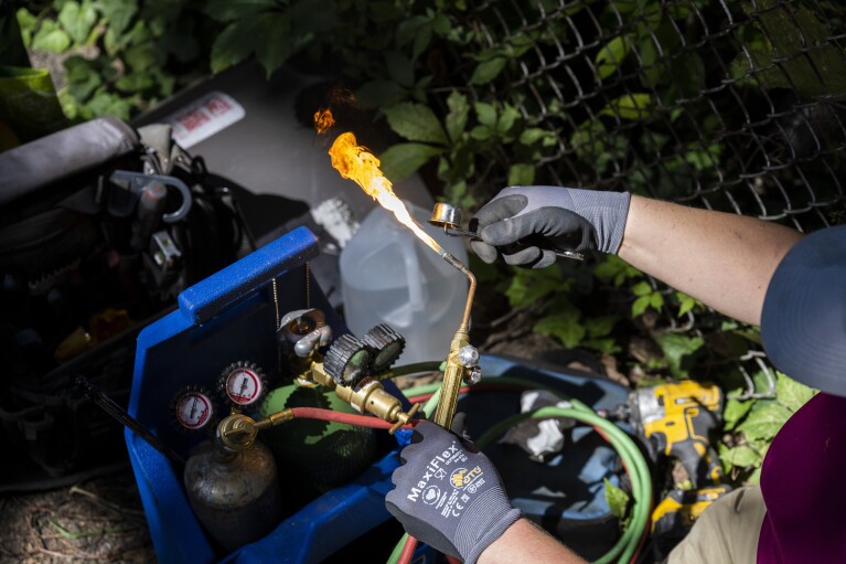 Jennifer Byrne, owner and technician at Comfy Heating and Cooling, prepares a torch to repair an air conditioning condenser unit in Philadelphia on Thursday, Sept. 14, 2023. (AP Photo/Joe Lamberti)