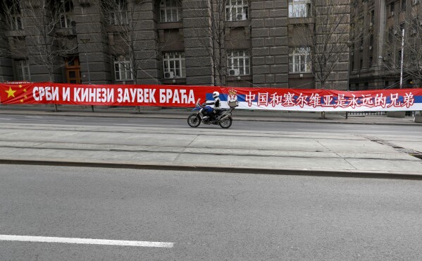 FILE - A motorcyclist rides past a billboard showing Serbian and Chinese flags that read: "Serbs and Chinese brothers forever" placed on a street prior to a curfew set up to help prevent the spread of the new coronavirus in Belgrade, Serbia, Monday, April 13, 2020. Chinese President Xi Jinping will visit France, Serbia and Hungary next week as Beijing appears to seek a larger role in the conflict between Russia and Ukraine that has upended global political and economic security. (AP Photo/Darko Vojinovic, File)