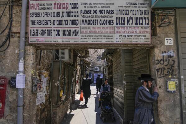 Ultra-Orthodox Jews walk past a sign calling on women to dress modestly in the ultra-Orthodox neighborhood of Mea Shearim in Jerusalem, Wednesday, June 7, 2023. With ultra-Orthodox parties now wielding unprecedented power and playing a key role in a contentious plan to overhaul the legal system, they are aggravating concerns among secular Israelis that the character and future of their country is under threat. (AP Photo/Ohad Zwigenberg)