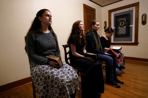 Estudiantes de Benedictine College, de izquierda a derecha, Madeline Hays, Niki Wood, Ashley Lestone y Hannah Moore se reúnen para las oraciones vespertinas en una habitación que convirtieron en capilla en la casa que comparten el domingo 3 de diciembre de 2023 en Atchison, Kansas. En Estados Unidos, la Iglesia católica está atravesando un inmenso cambio. Generaciones de católicos que abrazaron la marea modernizadora están dando paso cada vez más a conservadores religiosos que creen que el cambio ha torcido la Iglesia. (Foto AP/Charlie Riedel)