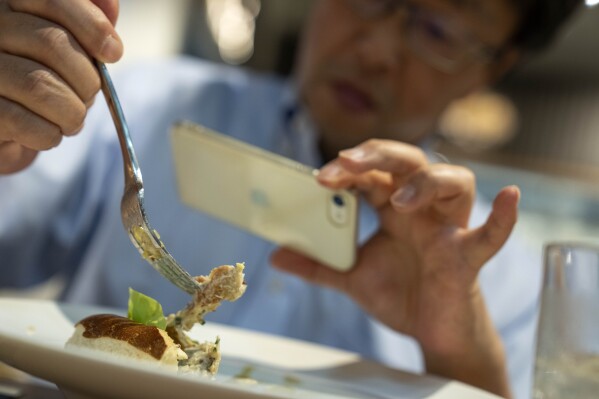 Nobuhisa Kawaguchi takes a picture of lab cultivated chicken from GOOD Meat during a tasting at Huber's Butchery in Singapore, Wednesday, July 12, 2023. Singapore was the first nation to authorize the sale of meat cultured from cells in a bioreactor. A chef there offers a tasting menu every week. (AP Photo/David Goldman)