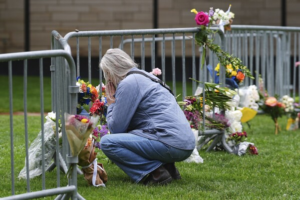 A visitor offers a tribute after leaving a bouquet of flowers at a makeshift memorial for victims of an attack outside of the Boulder County, Colo., courthouse as a light rain falls Tuesday, June 3, 2025, in Boulder, Colo. (AP Photo/David Zalubowski)